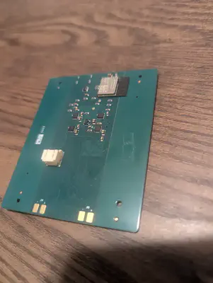 An assembled green circuit board on a wooden table, with a radio module, its antenna, and a white connector