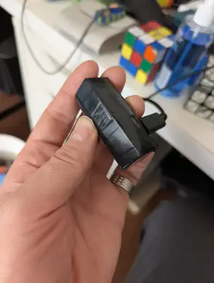 Un petit bloc rectangulaire noir entouré de ruban, tenu dans une main, avec un câble USB-C branché à une extrémité