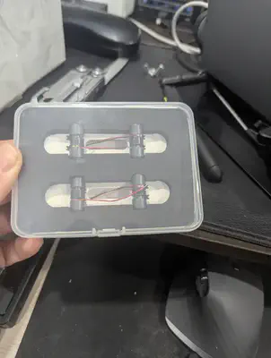 Un boîtier en plastique transparent tenu dans une main, avec quatre petits actionneurs cylindriques noirs TITAN Haptics logés dans des découpes de mousse, chacun avec de fins fils rouge et noir
